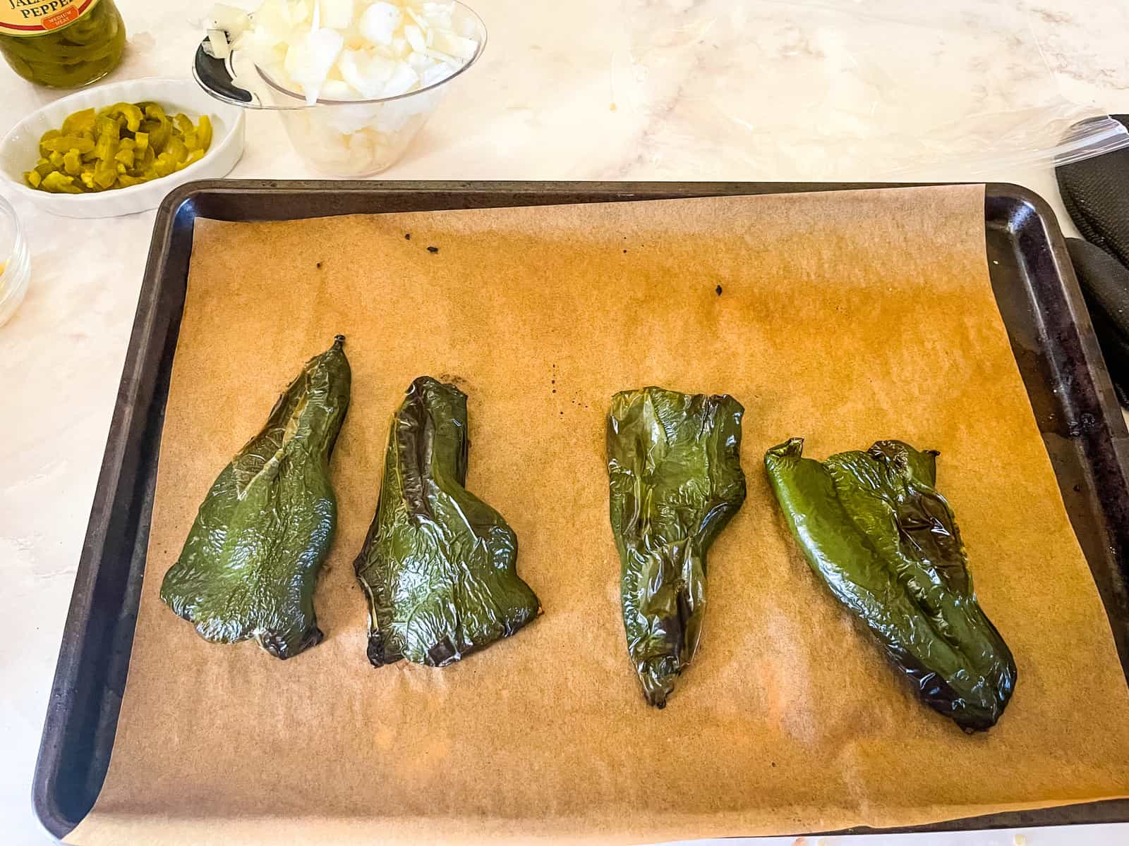 four roasted poblano pepper halves on a parchment lined baking sheet