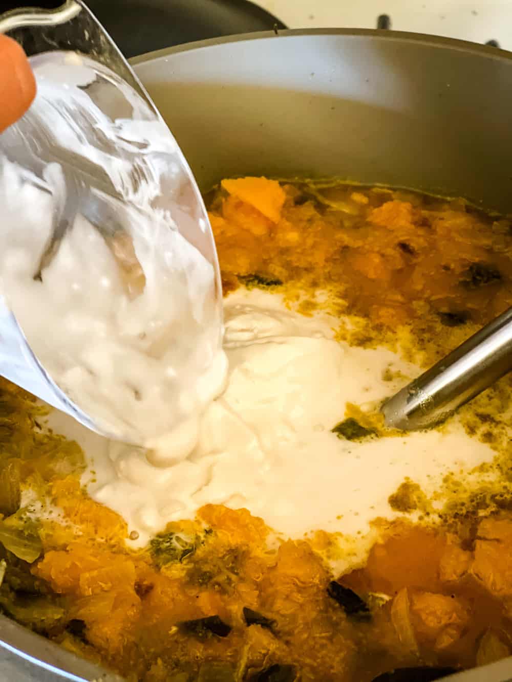 pouring coconut cream into butternut squash soup