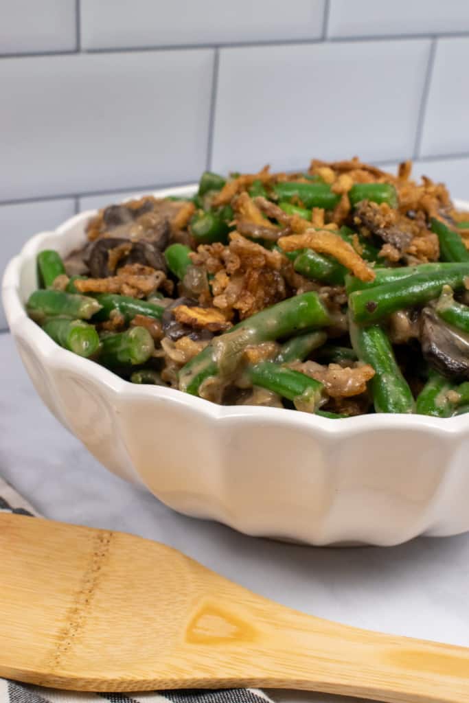 cooked green bean casserole in white casserole dish with wooden spoon to the side