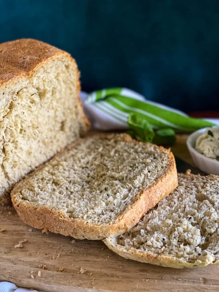 baked loaf of olive oil herb bread with slices on a cutting board