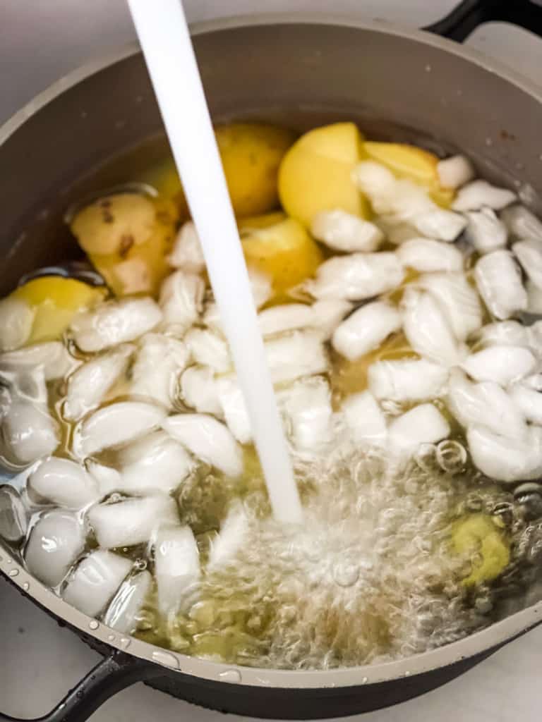boiled potatoes cooling down in ice water with a stream of tap water as well