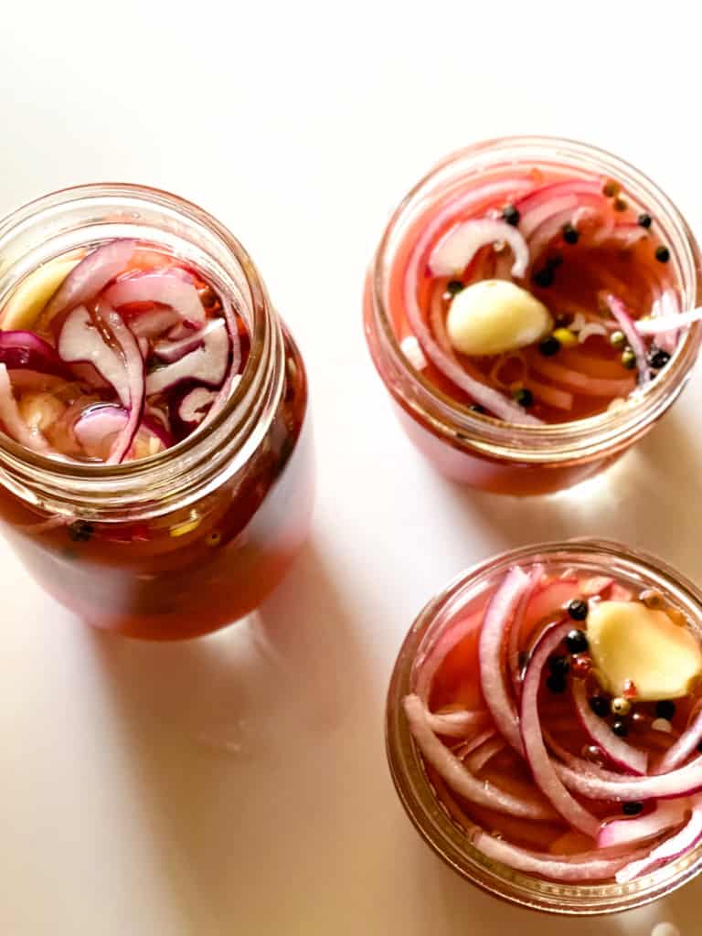 three jars with sliced onions peppercorns and garlic filled with liquid