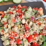 prepared quinoa salad with chickpeas on a dark slate plate with sliced cucumber, and cherry tomatoes in background with fork in salad
