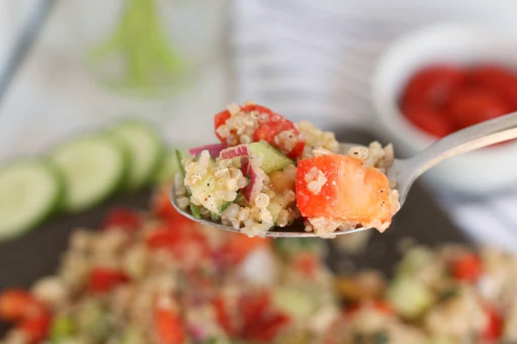 prepared quinoa salad with chickpeas on a dark slate plate with sliced cucumber, and cherry tomatoes in background with forkful of salad