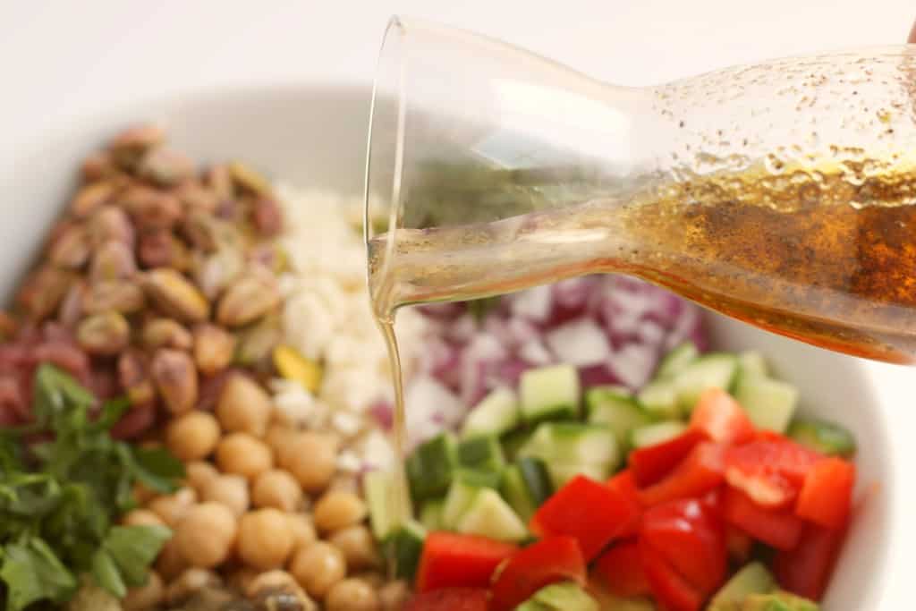 pouring vinaigrette over quinoa salad ingredients