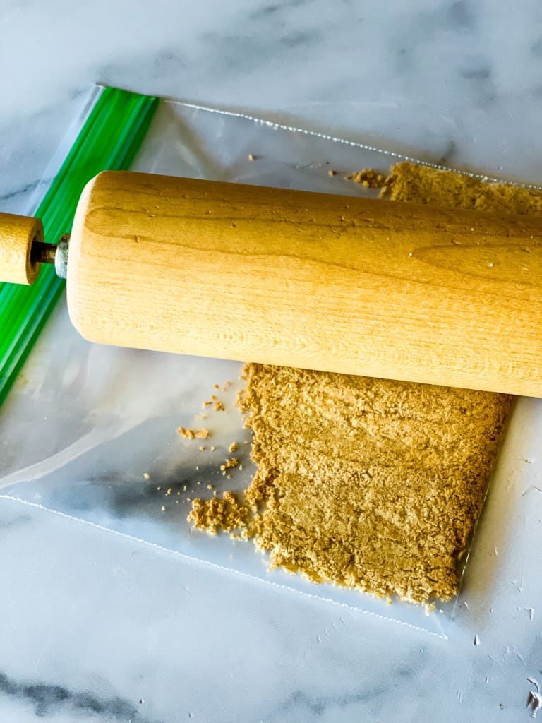 rolling pin over a plastic bag with graham cracker inside