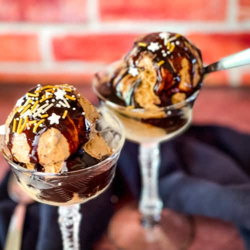 vegan haagen daz coffee ice cream copycat in glass goblets with red brick background with chocolate sauce and sprinkles