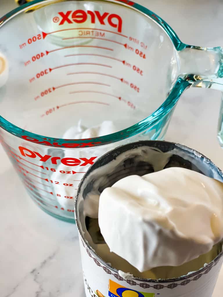 measuring out coconut cream into glass measuring cup