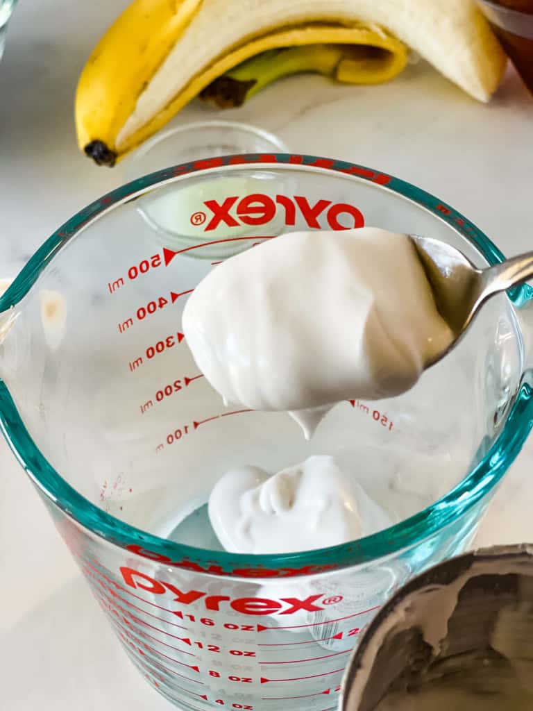 measuring out coconut cream into glass measuring cup