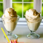 two glass ice cream dishes with pina colada ice cream in front of a window with two umbrella straws in foreground