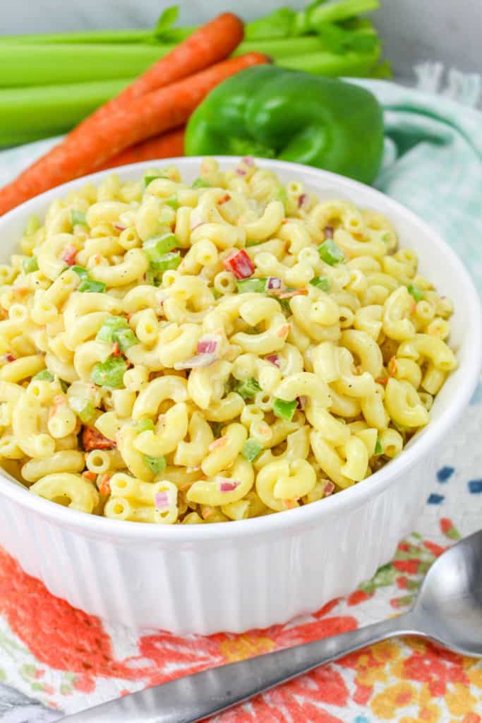 bowl of vegan macaroni salad with carrots, green pepper, and celery in the background