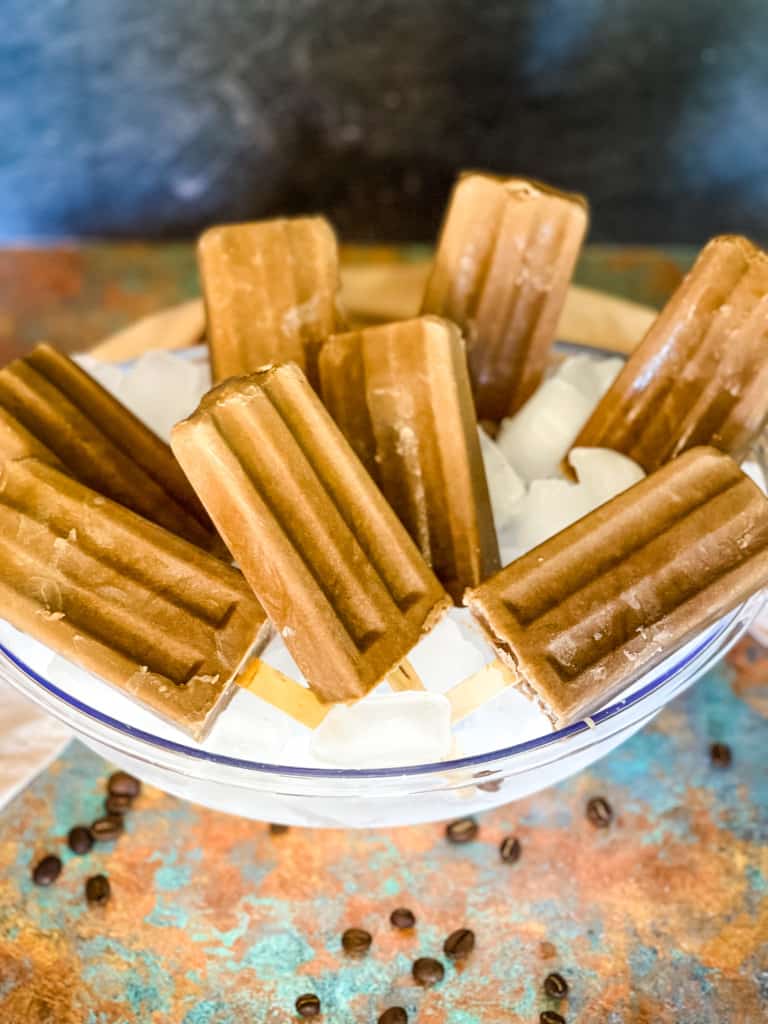 creamy coffee popsicles in bowl of ice with a few coffee beans scattered on around