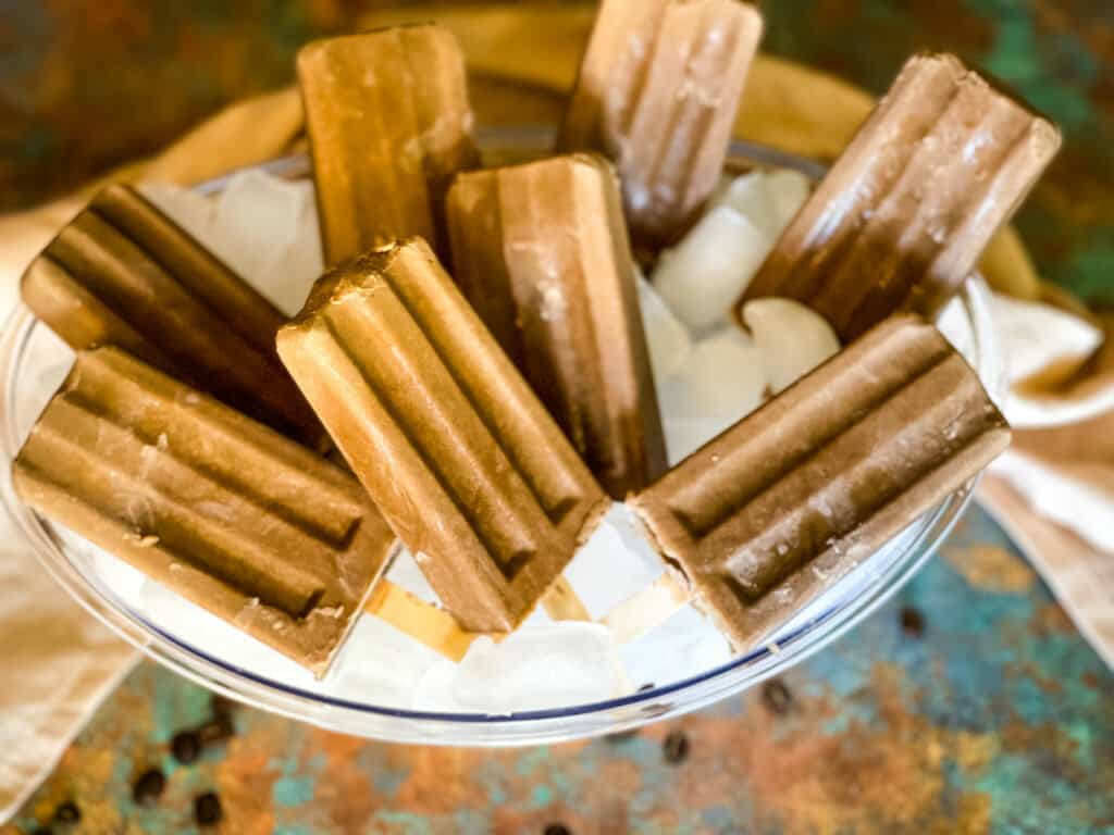 creamy coffee popsicles in bowl of ice with a few coffee beans scattered on around