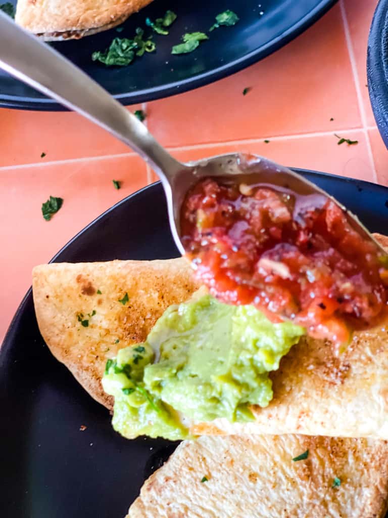 spooning salsa and guacamole on the tiny tacos