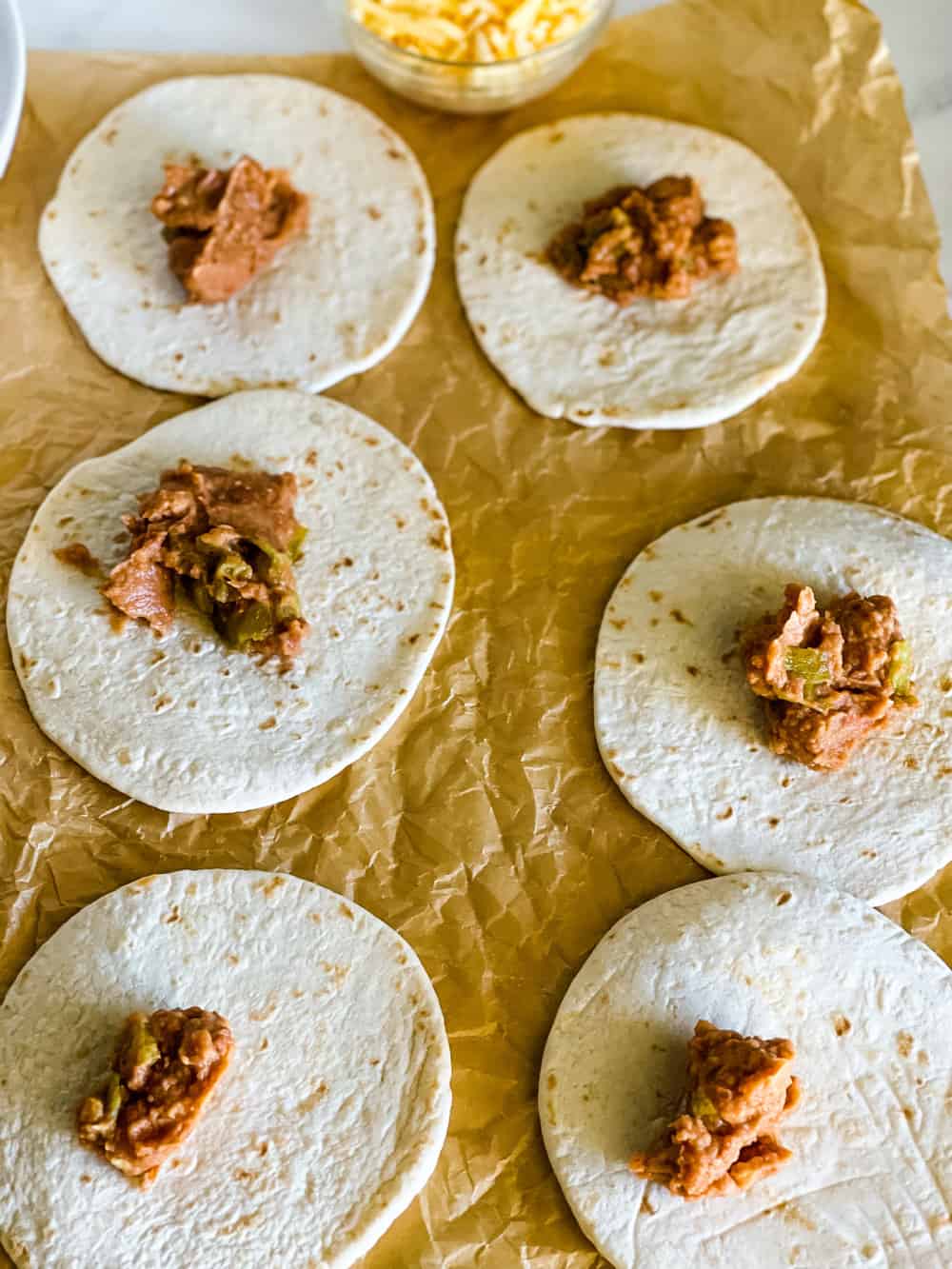 six small tortillas with a spoon full of refried beans in the center of each