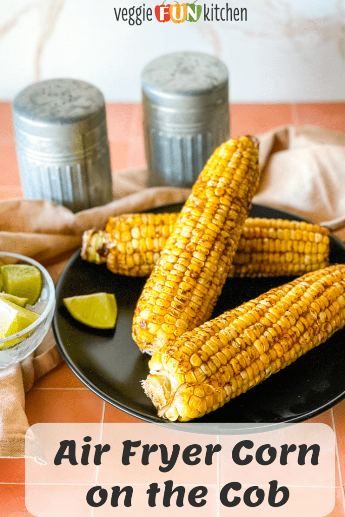 four air fryer corn on the cob on black plate with lime on side and salt and pepper shaker in the background with pinterest text overlay