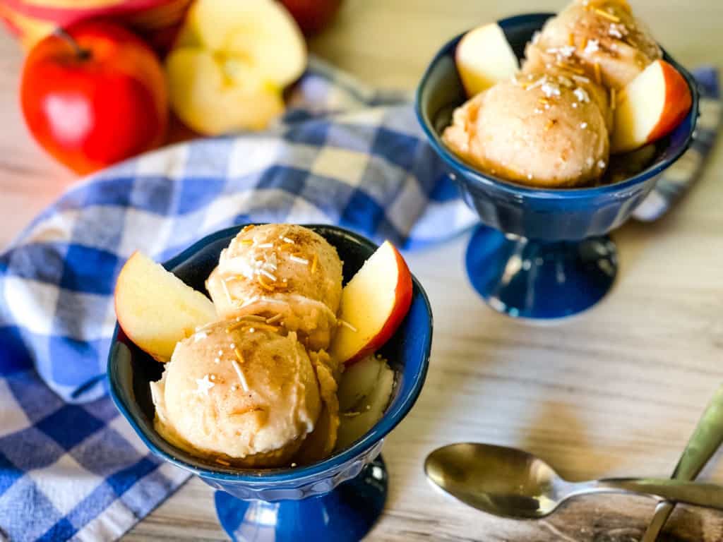 apple pie ice cream in two blue dishes with sprinkles on top and apple slices on the side
