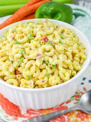 bowl of vegan macaroni salad with carrots, green pepper, and celery in the background