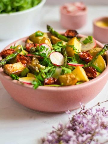 bowl of roasted potato salad with oil, dressing and vegetables on the side