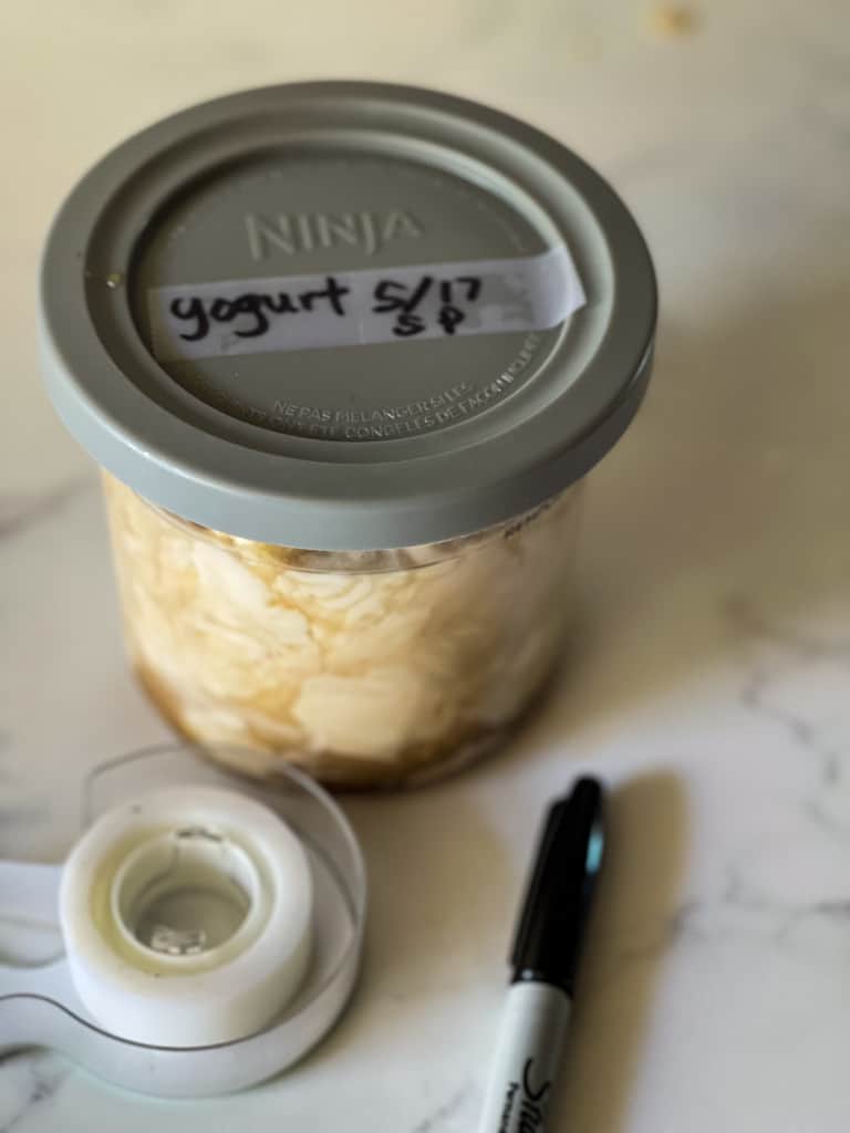 ninja creami container with lid showing name of recipe and date written with sharpie marker with marker and tape in foreground