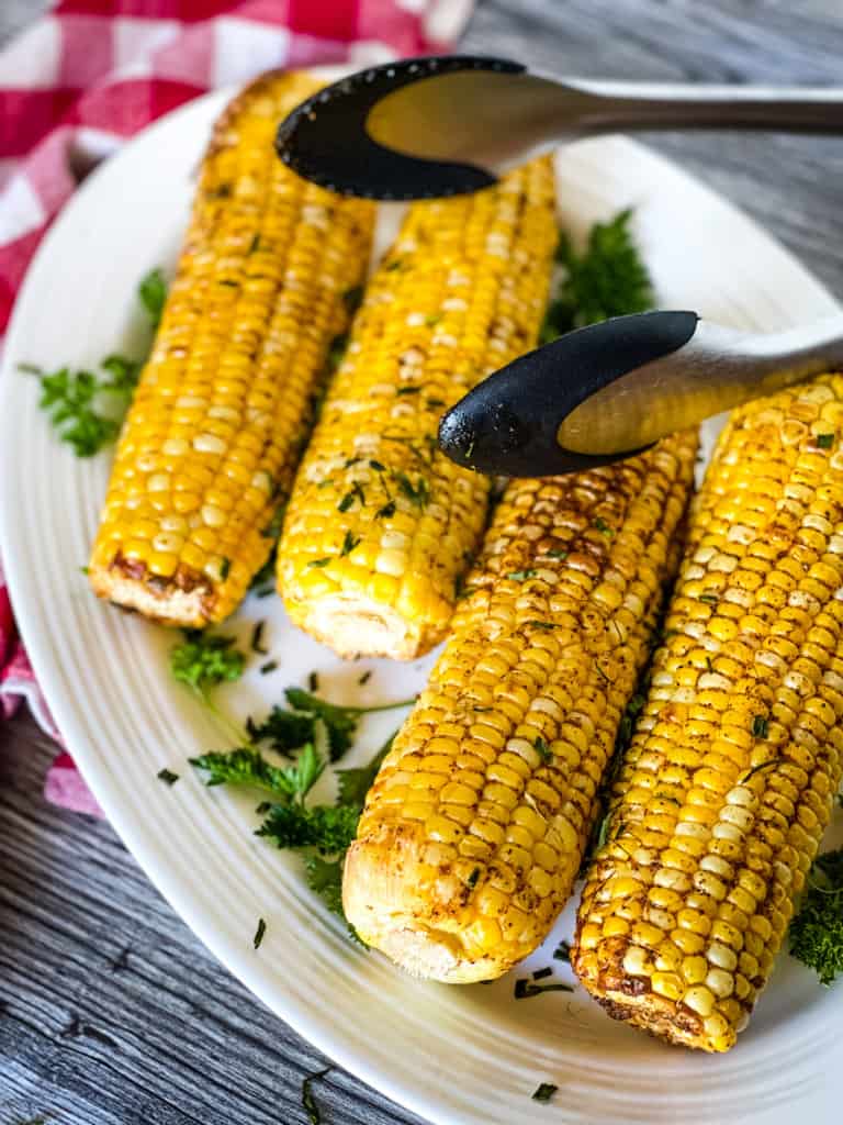 four corn on the cob on white plate with tongs