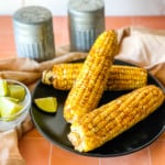 four air fryer corn on the cob on black plate with lime on side and salt and pepper shaker in the background