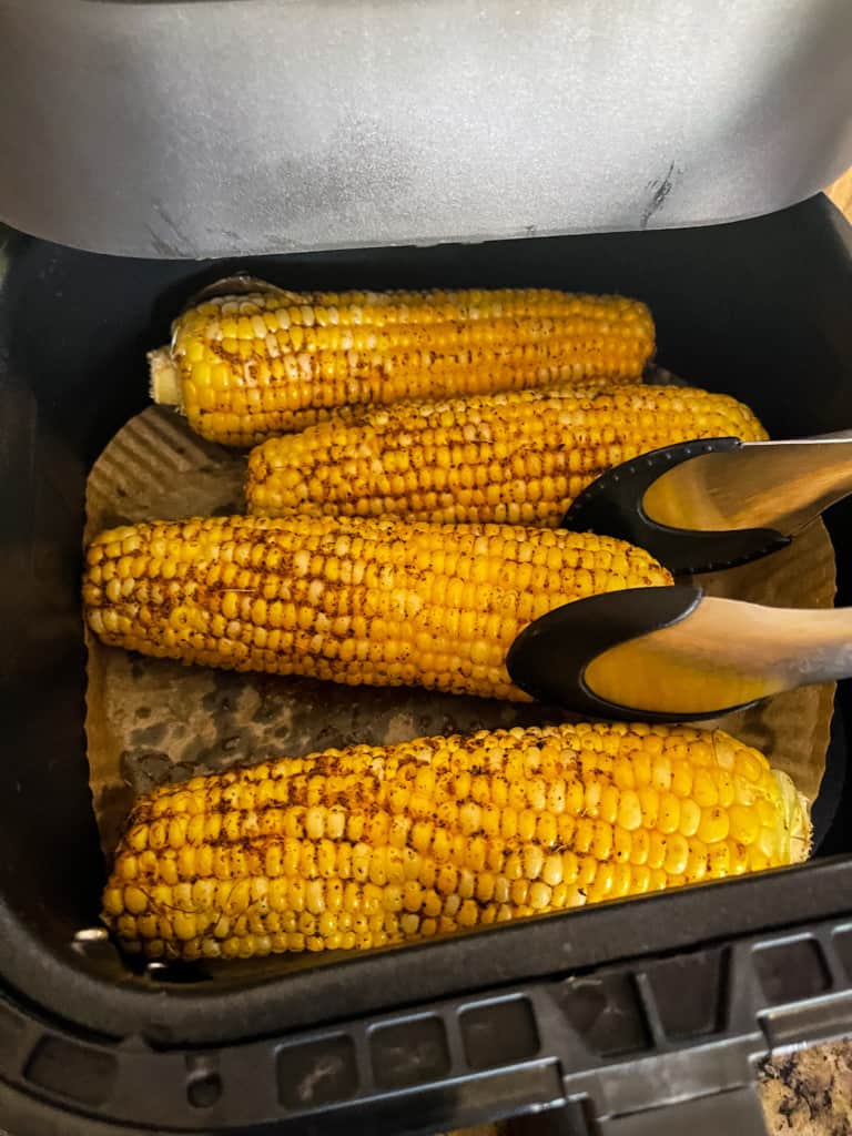 turning corn with corn in air fryer with tongs