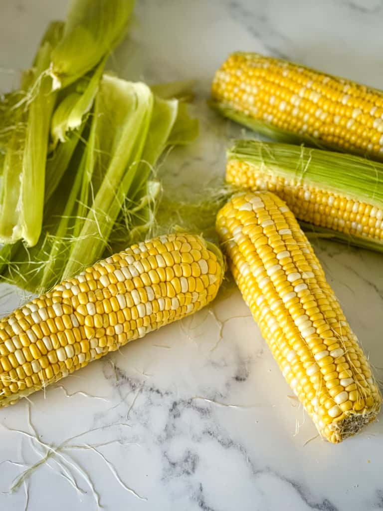 four corn on the cob being shucked