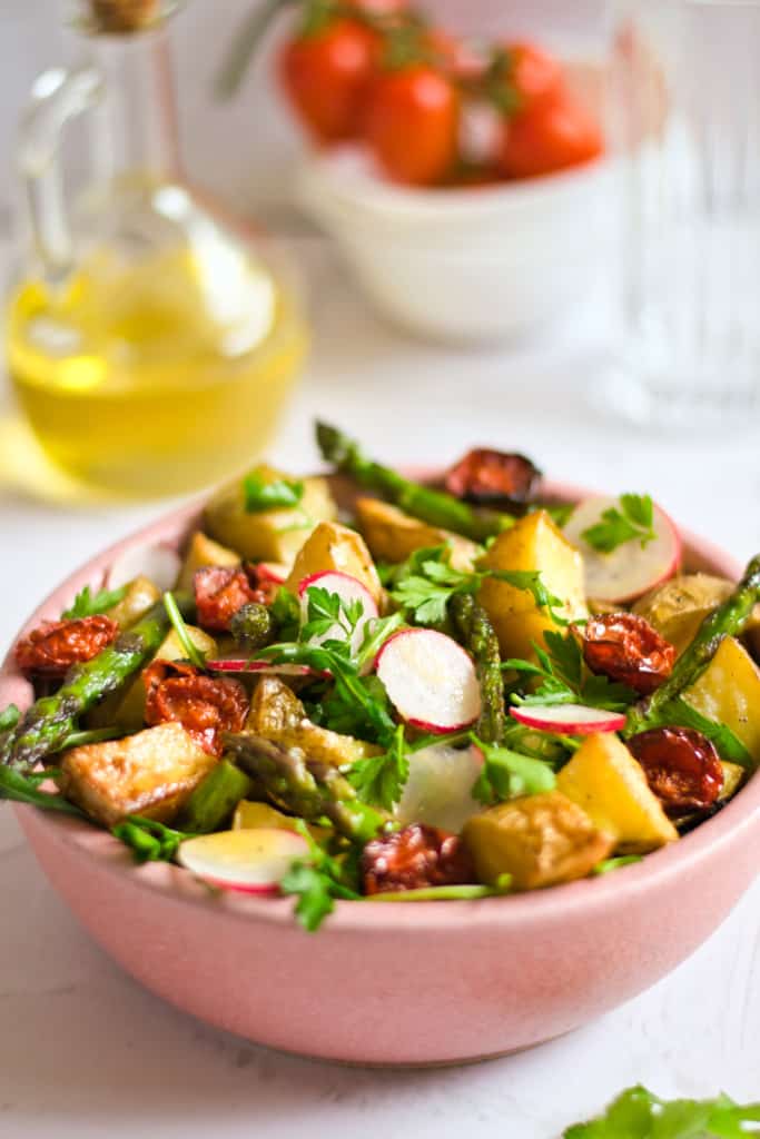 bowl of roasted potato salad with oil, dressing and vegetables on the side