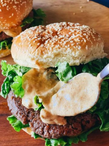 spooning sauce onto two vegan burgers showing vegan burger sauce