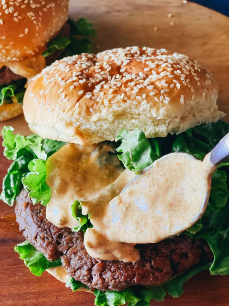 spooning sauce onto two vegan burgers showing vegan burger sauce