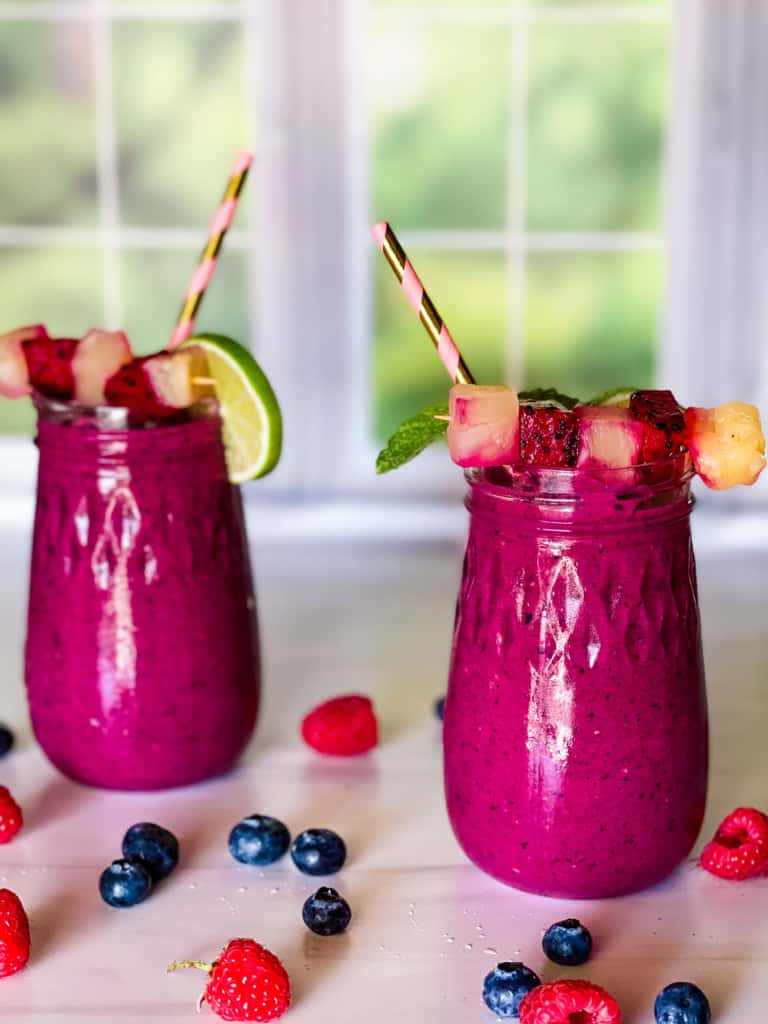 two glasses of dragon fruit smoothies with garish on top and berries scattered around