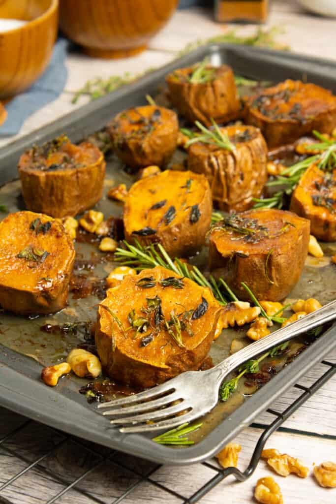 sweet potato rounds on baking sheet with fork in corner with rosemary