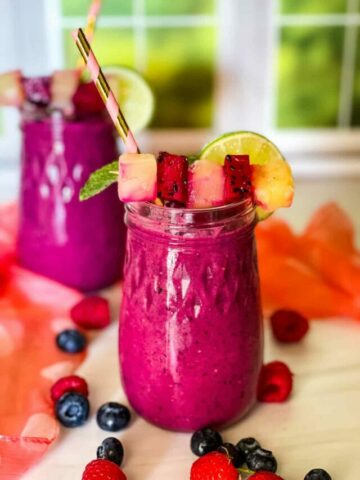 two glasses of dragon fruit smoothies with garish on top and berries scattered around