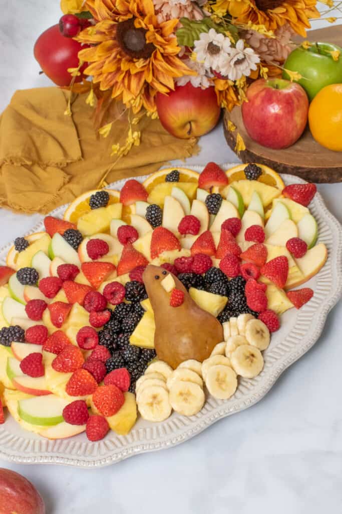 completed turkey fruit tray with other fruit in background along with fall flowers