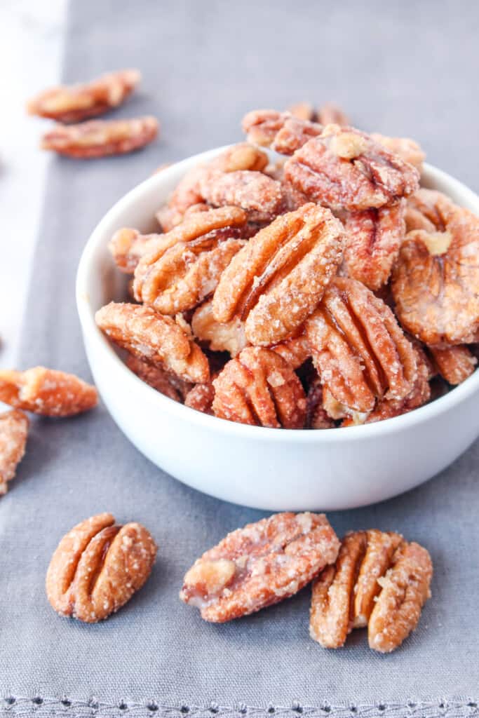 candied pecans in white bowl on grey cloth on round white table