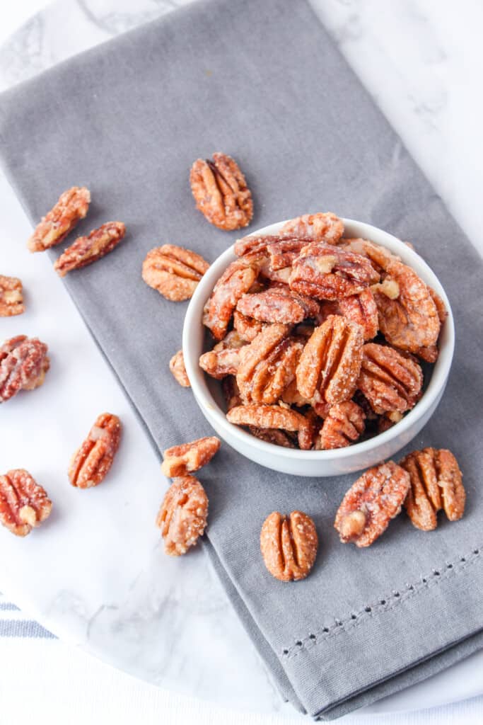 candied pecans in white bowl on grey cloth on round white table
