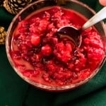 Bowl of raspberry Cranberry sauce with spoon in bowl and pinecones and grapes in background