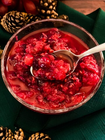 Bowl of raspberry Cranberry sauce with spoon in bowl and pinecones and grapes in background