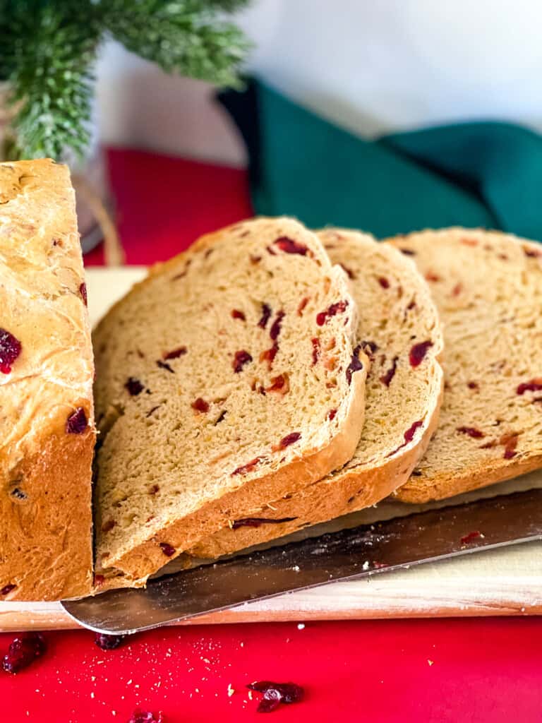 sliced orange cranberry bread with knife in foreground and christmas greenery in background