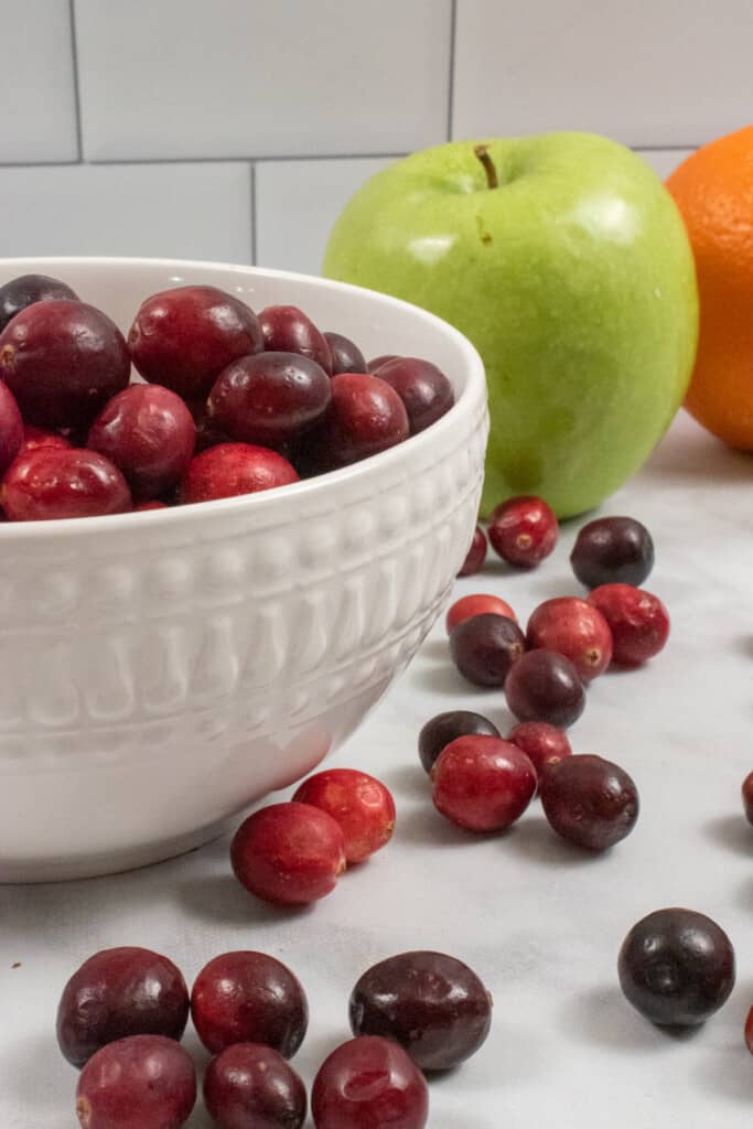 white bowl of cranberries with granny smith apple and orange at the side