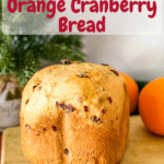loaf of orange cranberry bread on wooden cutting board with dried cranberries in foreground, two oranges and christmas greenery in background with pinterest text overlay