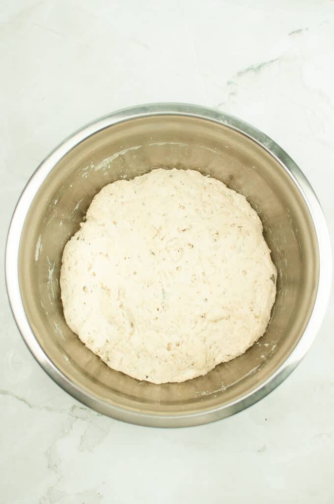 dough ball of rosemary garlic bread risen in metal bowl