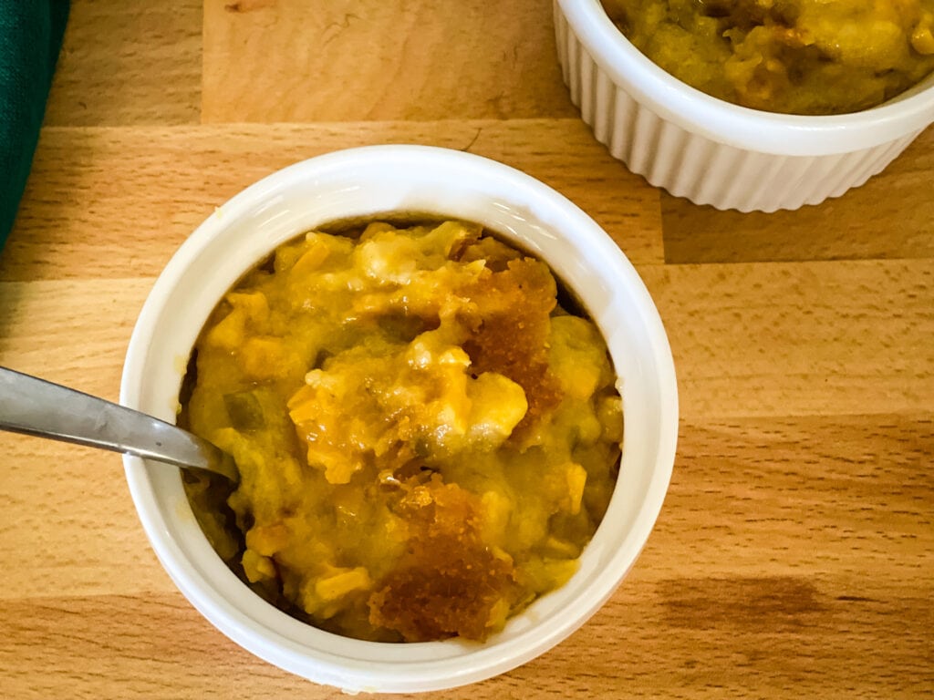 two white bowls of corn casserole with spoon