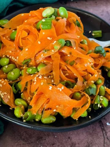 plated raw carrot salad with edamame with some on fork