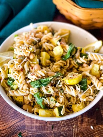 bowl of summer squash pasta with green napkin and bread basket in background