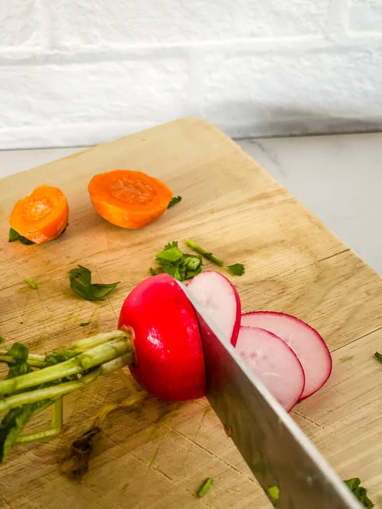slicing radishes with a knife with carrot tops in background