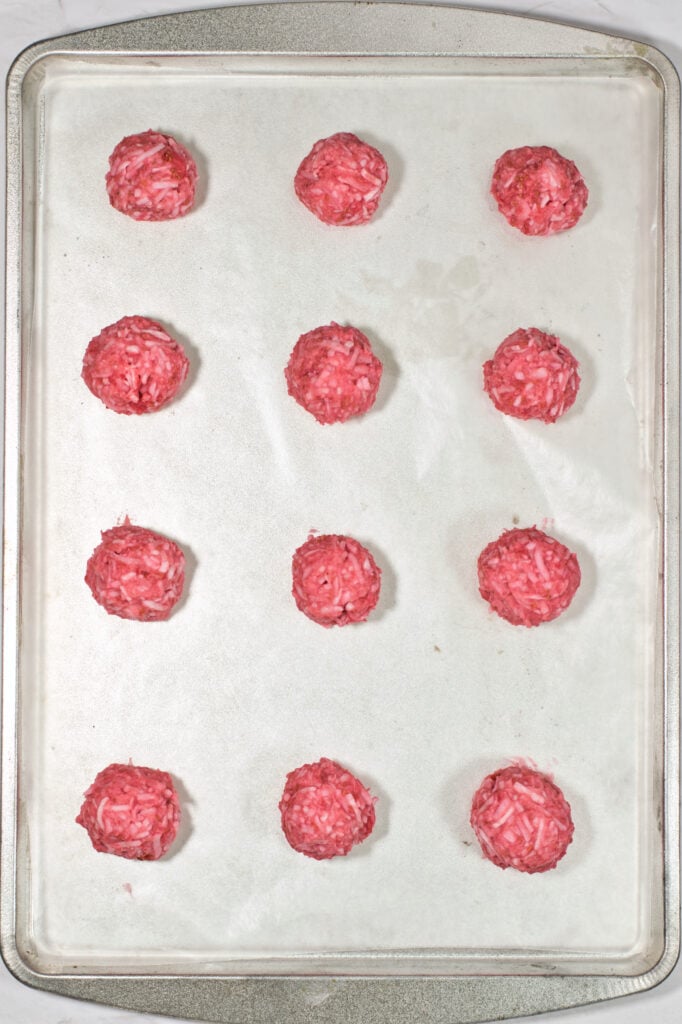 Baking tray with twelve rolled raspberry coconut truffles ready for dipping.