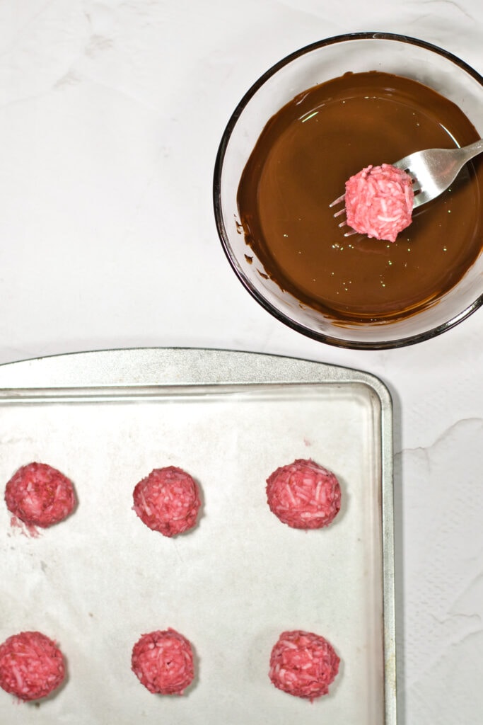 Dipping a raspberry truffle in chocolate with a fork with more ready for dipping in foreground