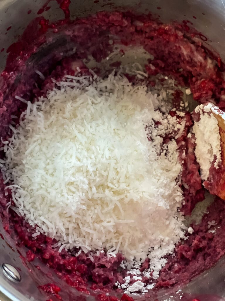 Mixing the coconut flakes and powdered sugar into the raspberry coconut butter mixture.